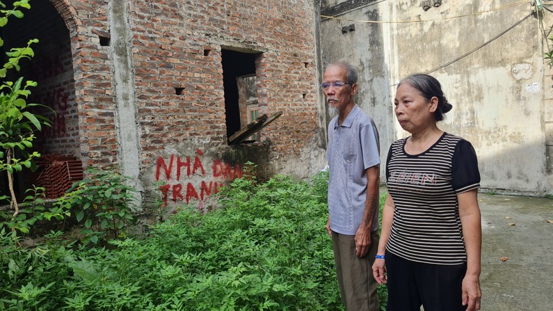 ông Lê Đình Đỡ và bà Lê Thị Hoàn thẩn thờ đứng trước thửa đất và ngôi nhà đang xây dang dở muốn bán nhanh thì vướng vào giao dịch thỏa thuận chuyển nhượng kéo dài nhiều năm