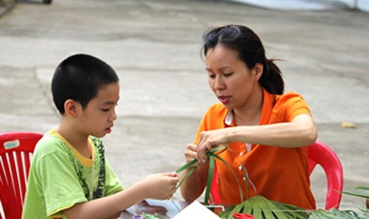 Được hướng dẫn, cậu bé hào hứng làm đồ chơi bằng lá.