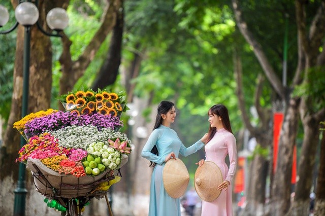 Những thiếu nữ với tà áo dài truyền thống bên những gánh hàng hoa đặc trưng của mùa Thu Hà Nội. (Ảnh: Điện tử Chính phủ)