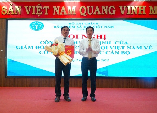 Phó Giám đốc BHXH Việt Nam Đào Việt Ánh (bên phải) trao quyết định và tặng hoa chúc mừng ông Nguyễn Viết Dũng.