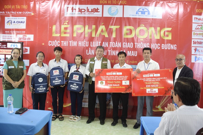 Ông Nguyễn Văn Nam – Đại diện phía Nam, Ban Truyền thông Đa phương tiện Báo Pháp luật Việt Nam, Phó Ban tổ chức Thường trực Đoàn Caravan (bên trái) cùng nhà tài trợ (bên phải) trao tặng bảng tượng trưng 700 ba lô cho học sinh Trường THCS Nguyễn Mai.