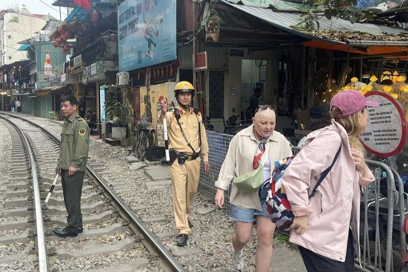 Du khách nước ngoài được CSGT mời di chuyển ra khỏi khu vực tàu chạy. (Nguồn: Công an TP Hà Nội) 